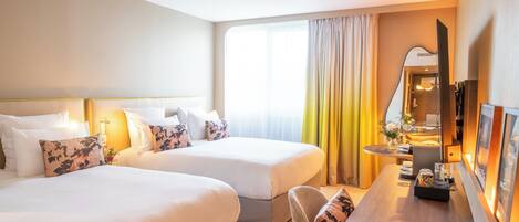 A hotel room with two beds, a desk, a chair, a TV, and a window with curtains.