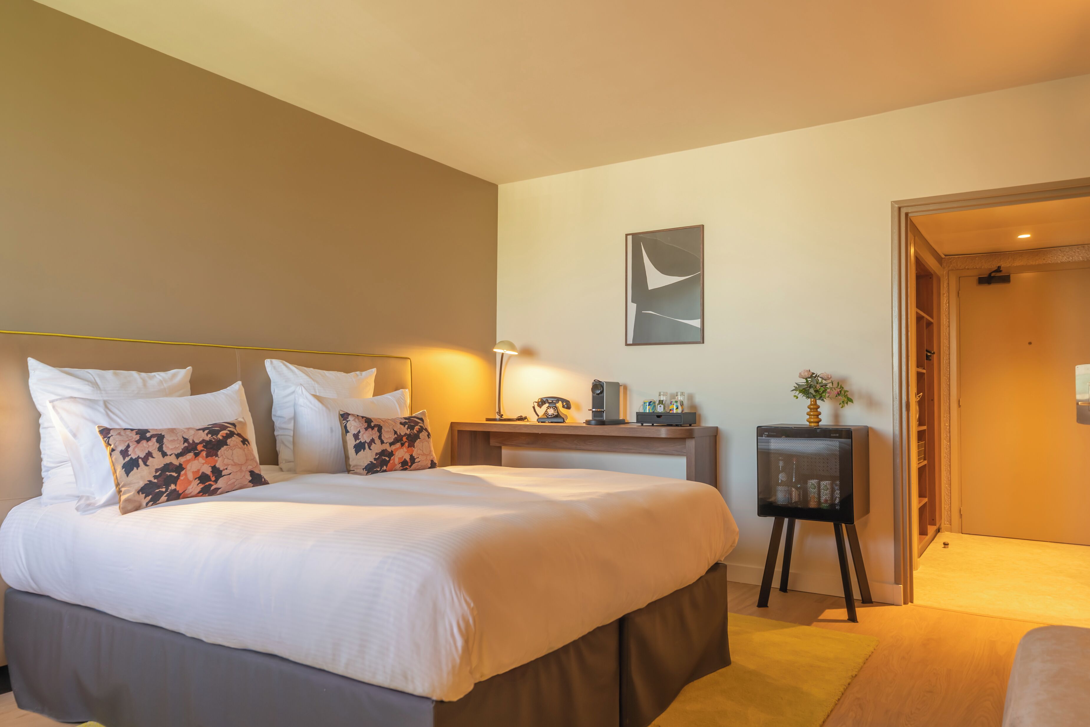 A hotel room with a large bed, bedside table, lamp, and a small cabinet.