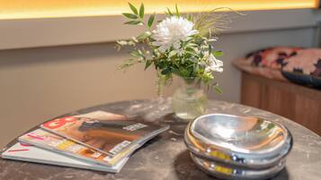Una mesa con un florero, una pila de revistas y un recipiente metálico.