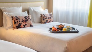 A neatly made bed with white linens and floral-patterned pillows, a tray with croissants, a cup, and a glass of juice on the bed.