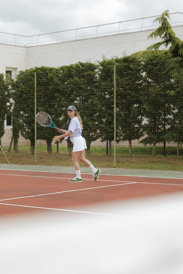 A tennis court with a chain-link fence, trees, and a building in the background.