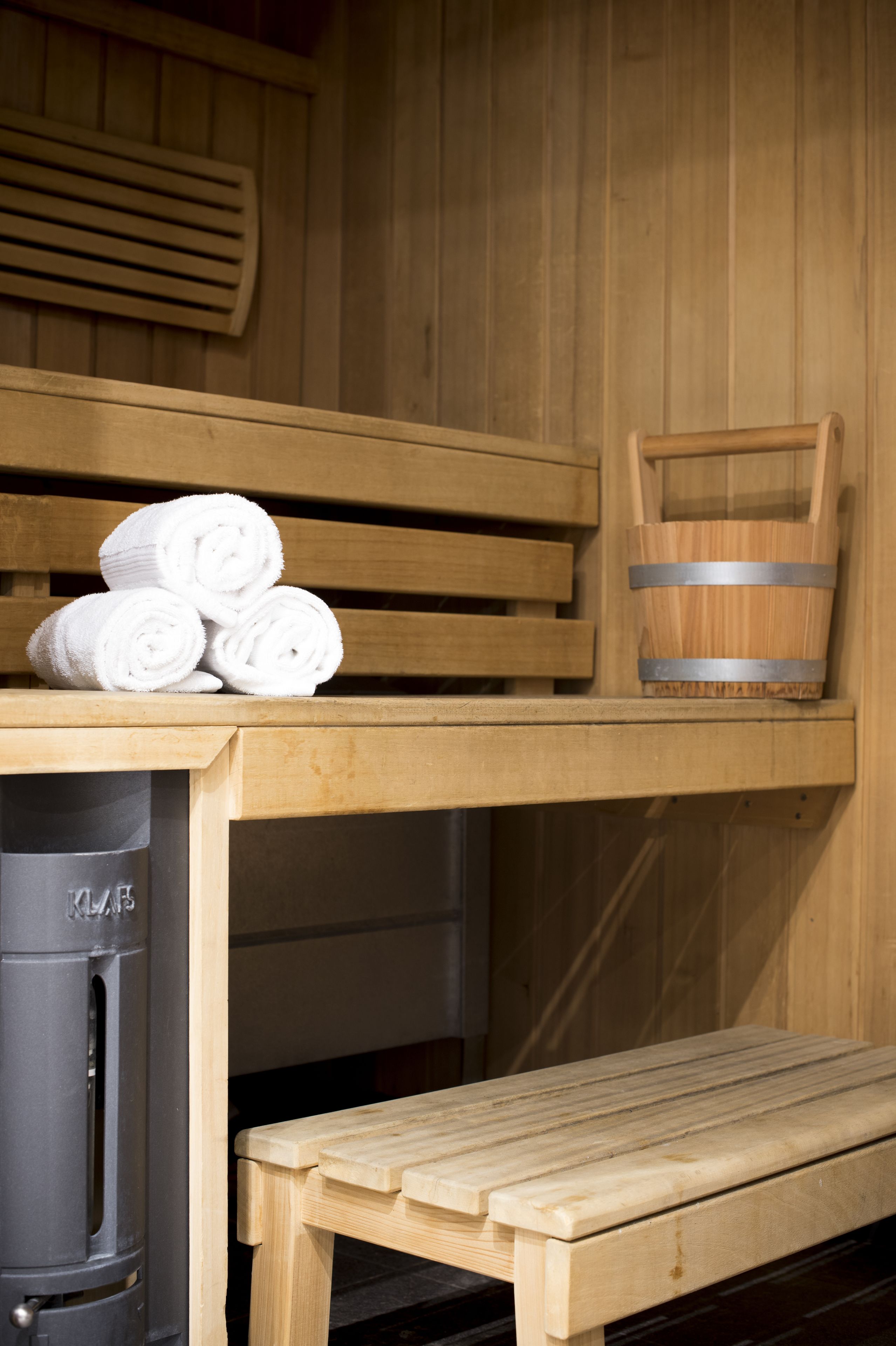 Un sauna avec des bancs en bois, un banc avec des serviettes et un seau en bois.