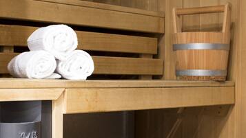 Un sauna avec des bancs en bois, un banc avec des serviettes et un seau en bois.