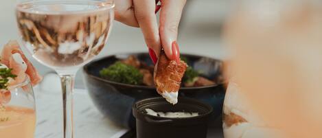 Una mesa de comedor con varios platos, una copa de vino blanco y una persona alcanzando la comida.