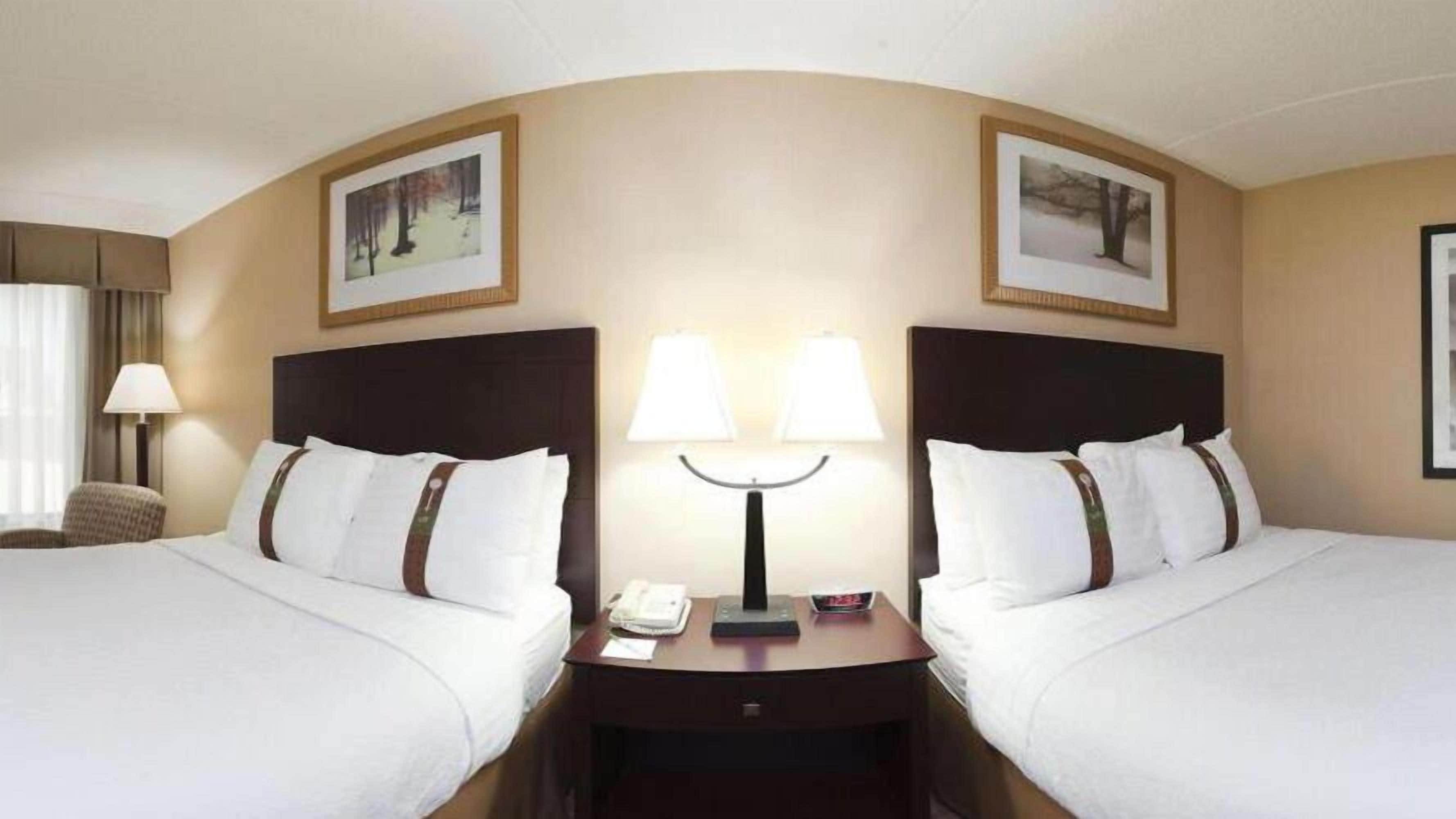 A hotel room with two beds, a nightstand with a lamp, and framed pictures on the wall.