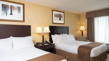 Quarto de hotel com duas camas, uma mesa de cabeceira com telefone e abajur, e duas imagens emolduradas na parede.