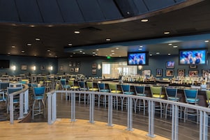 Zona de bar con diversas opciones de asientos, barra y televisores colgantes.