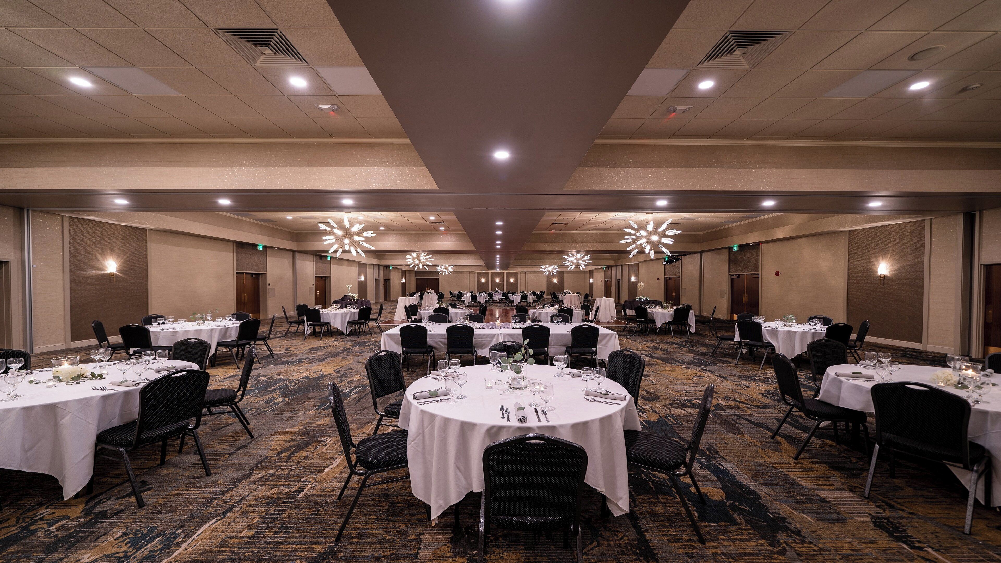 Un gran salón de banquetes con mesas redondas, sillas negras y manteles blancos.