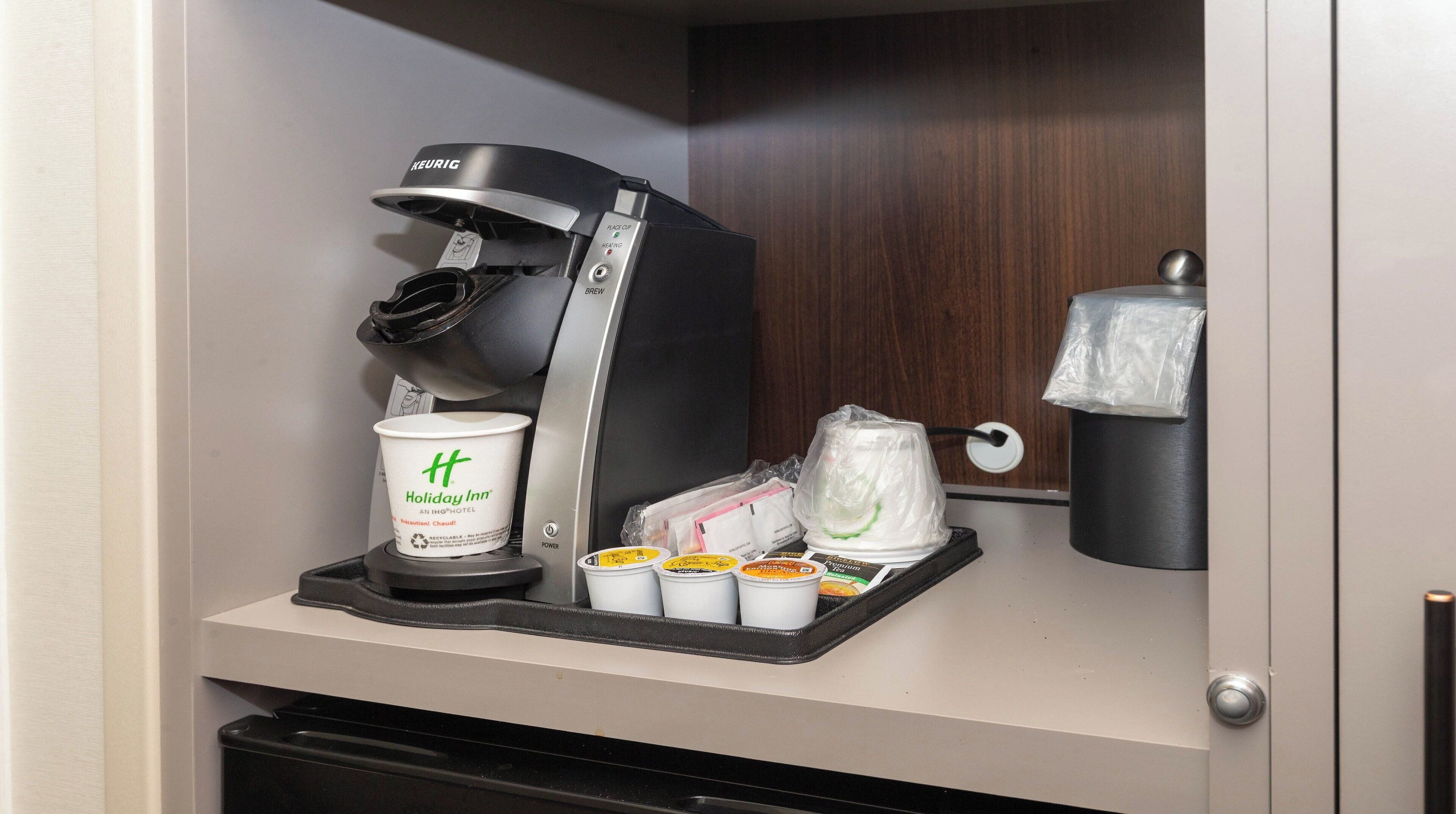 A coffee machine with a disposable cup and several small containers, likely for beverages, in a hotel setting.