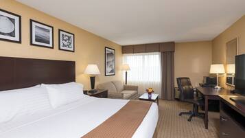 A hotel room with a large bed, a desk, a chair, a TV, and framed pictures on the wall.