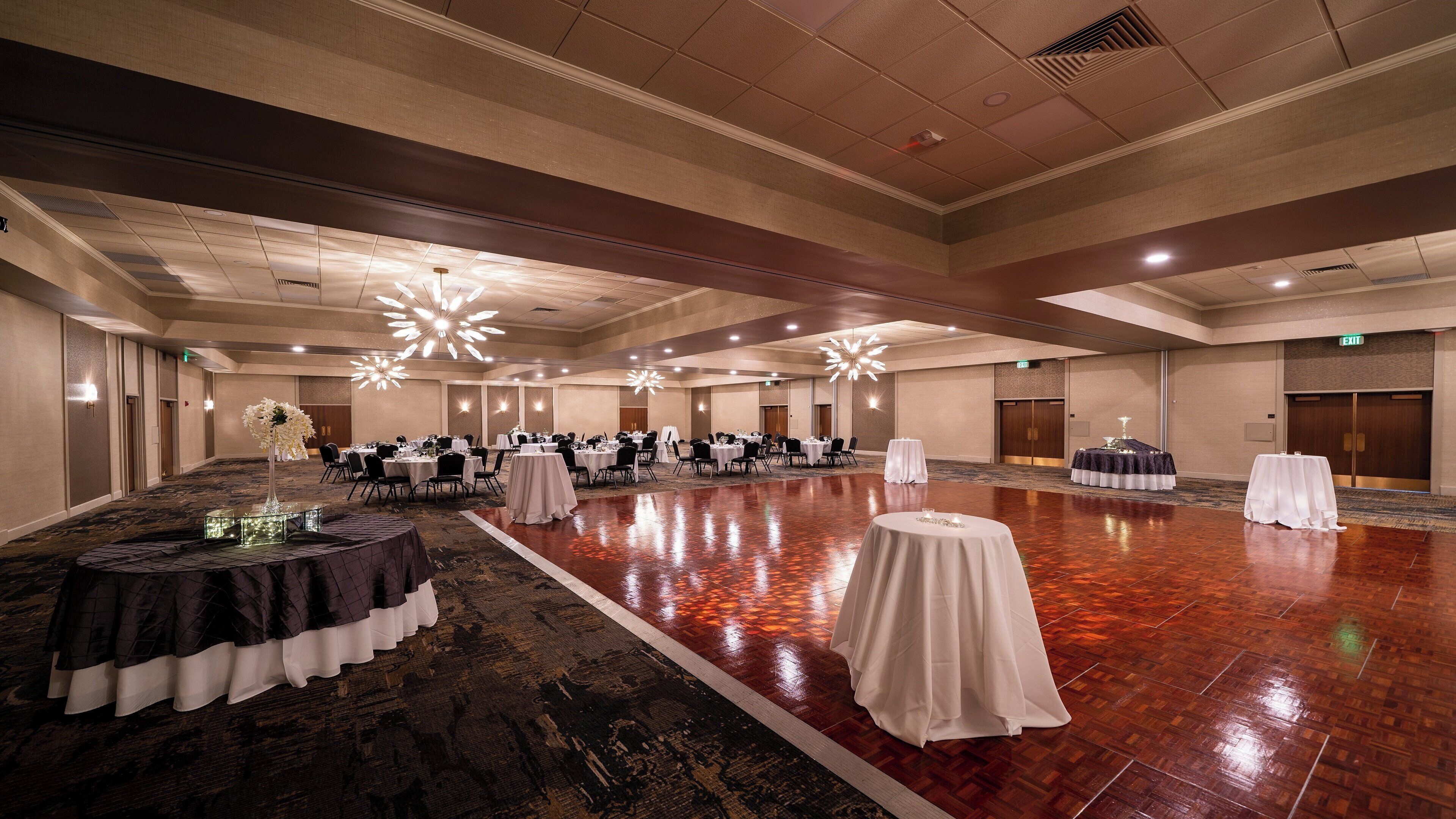 Un amplio y bien iluminado salón de banquetes con varias mesas redondas dispuestas para eventos.