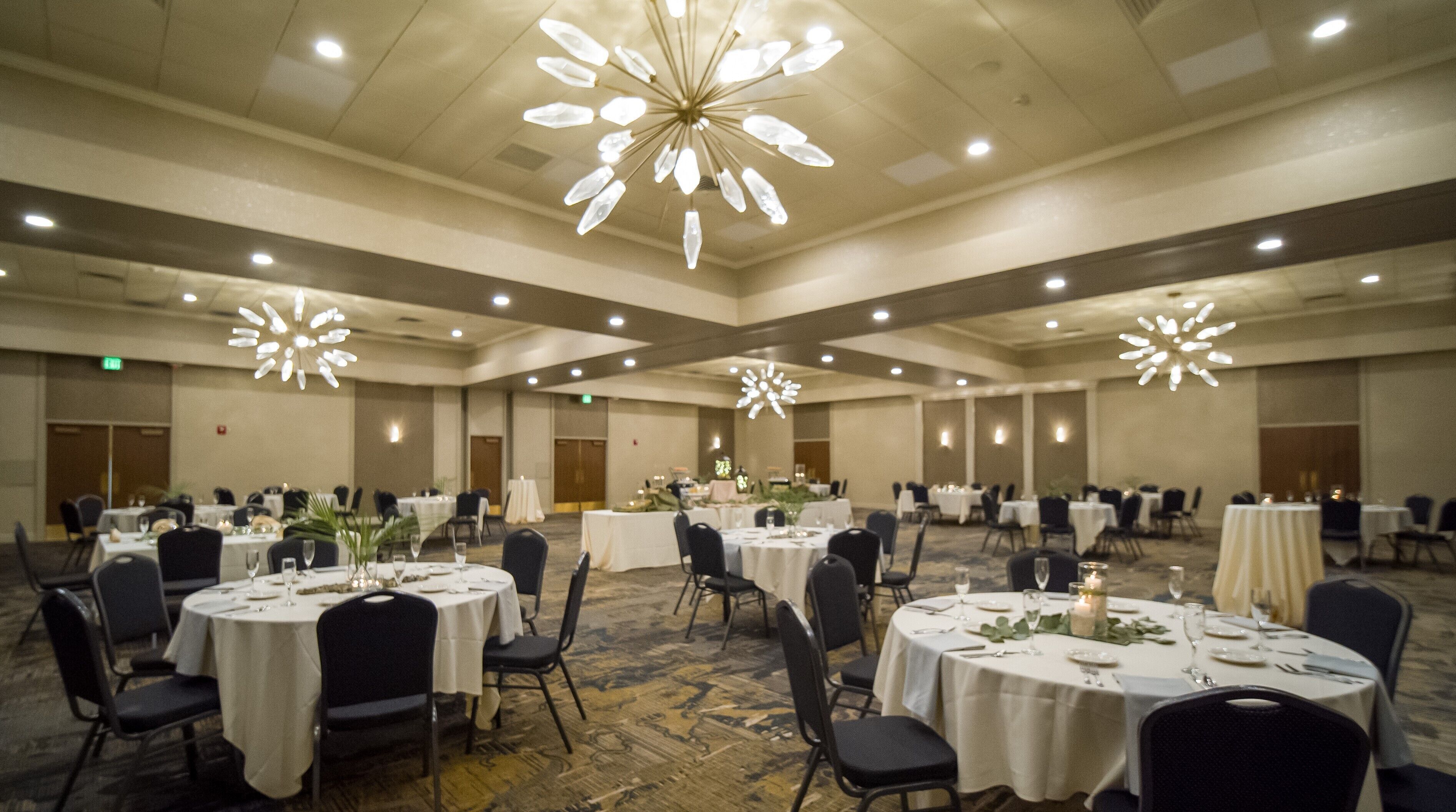 A banquet hall with round tables, chairs, and chandeliers.