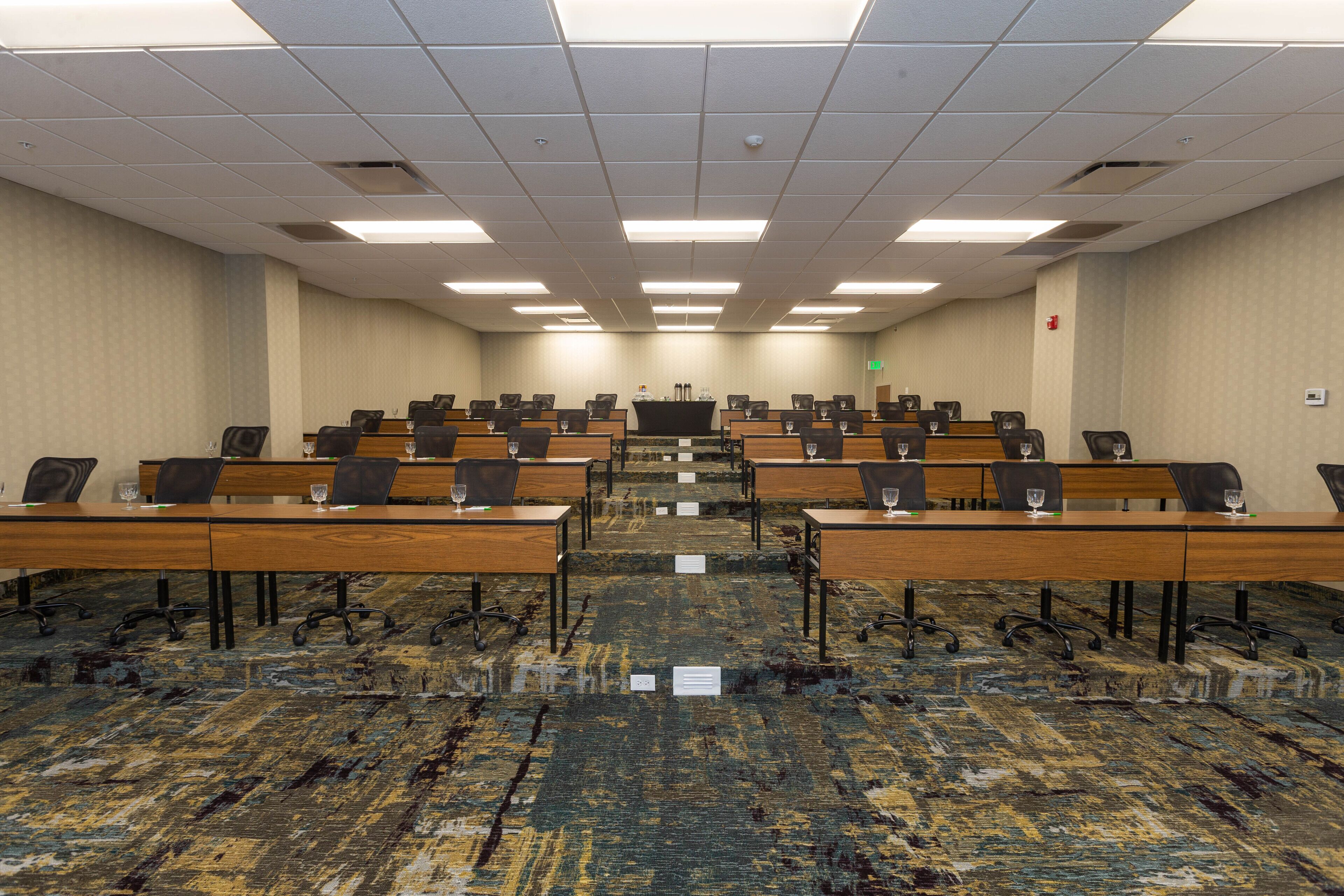 A conference room with rows of tables and chairs, carpeted floor, and a patterned wall.