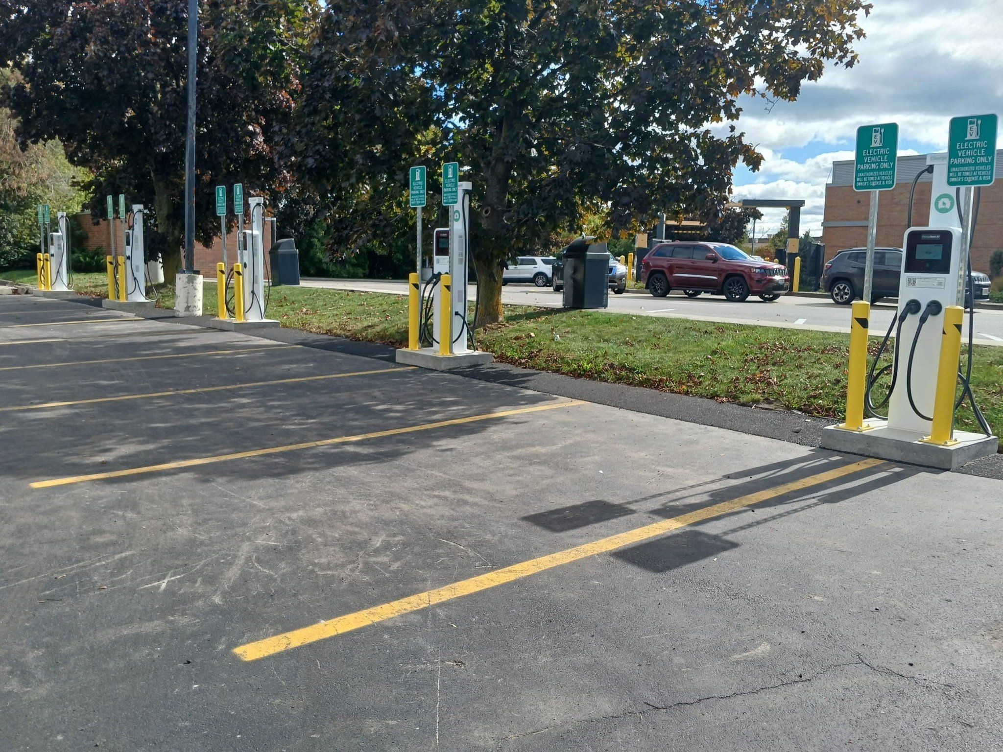 A parking area with electric vehicle charging stations, marked parking spaces, and a building in the background.