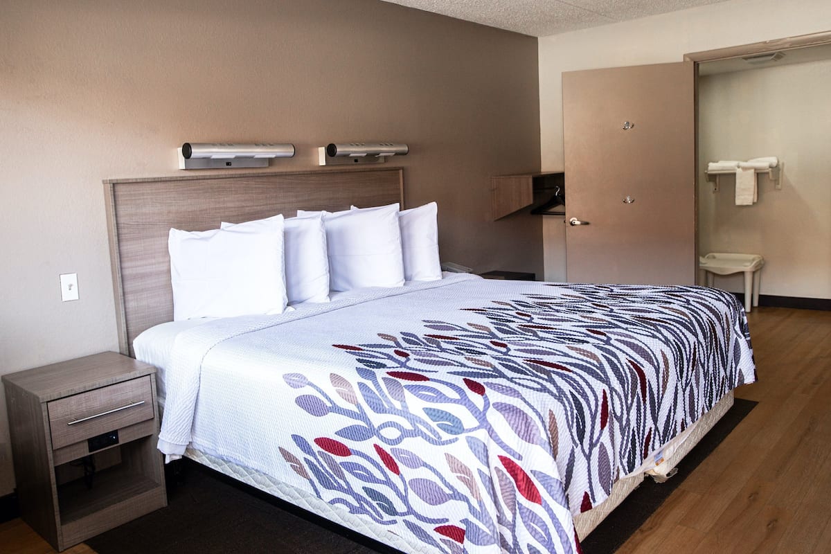 A hotel room with a bed, a nightstand, a wall-mounted air conditioner, and a door leading to a bathroom.