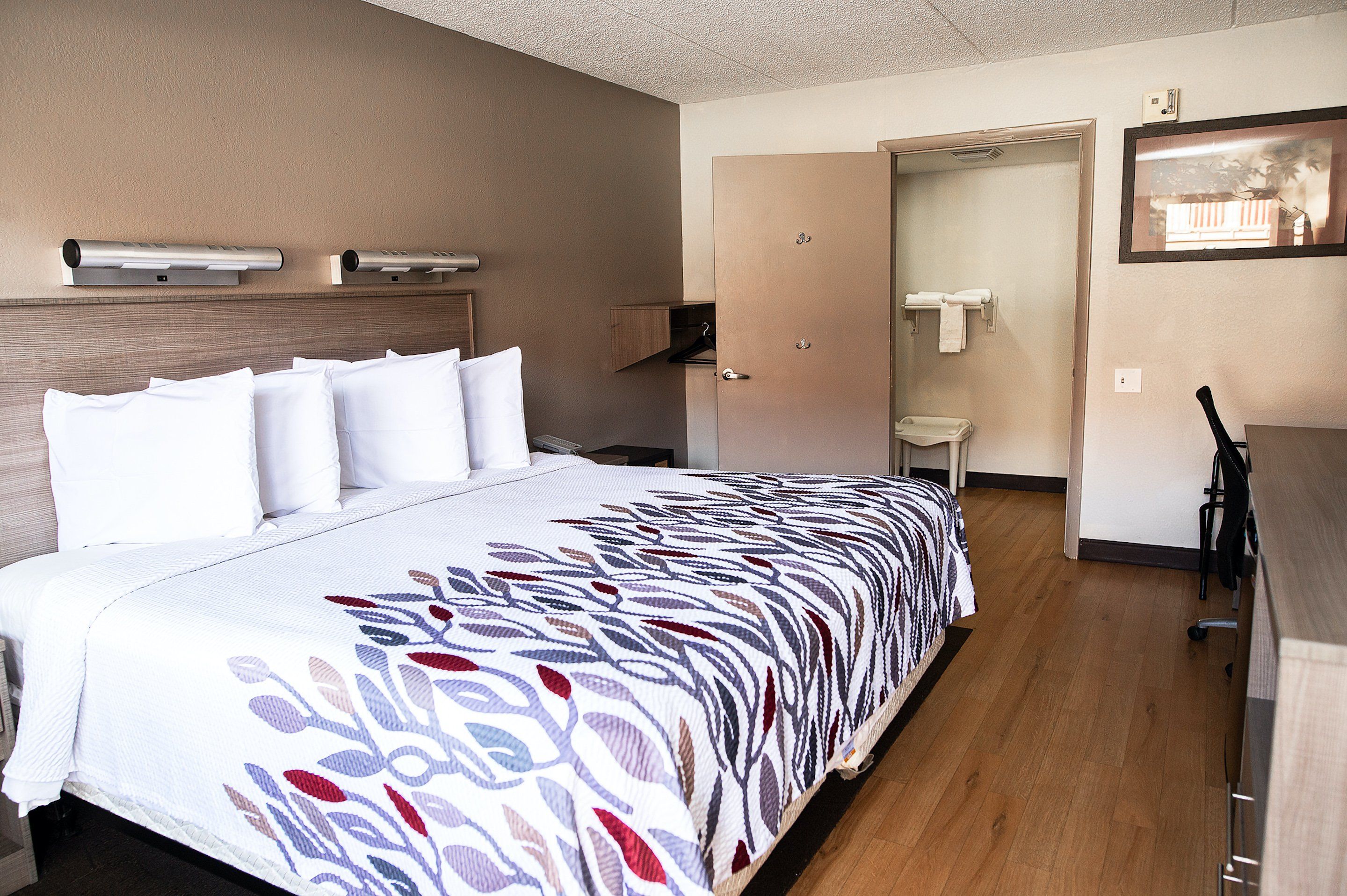 A hotel room with a bed, a desk, a chair, a wardrobe, and a door leading to a bathroom.