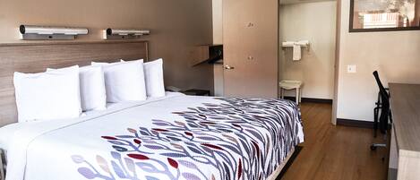 A hotel room with a bed, a desk, a chair, a wardrobe, and a door leading to a bathroom.