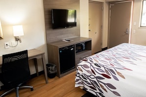 A hotel room with a bed, a desk, a television mounted on the wall, a microwave, and a trash can. - Red Roof Inn Rochester - Henrietta (Henrietta)