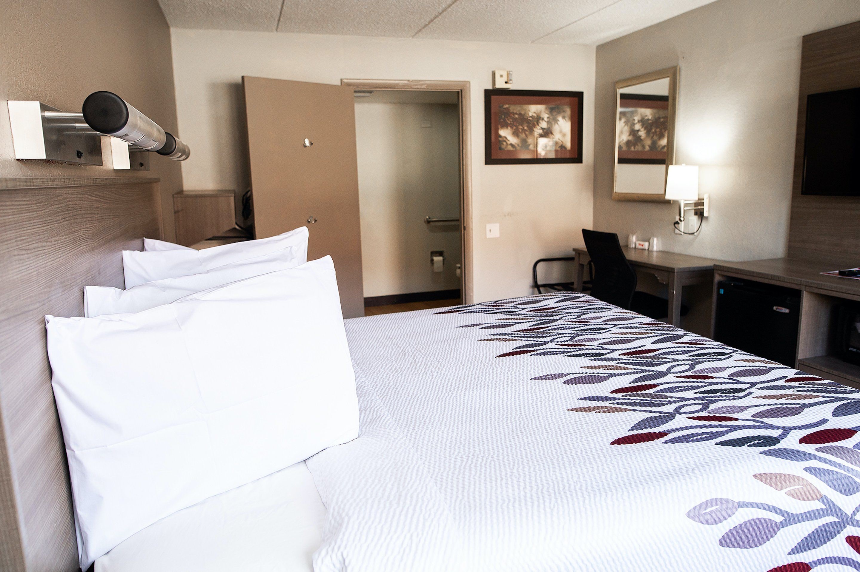 Ein Hotelzimmer mit einem großen Bett, einem Schreibtisch, einem Stuhl und einer Tür zu einem Badezimmer.