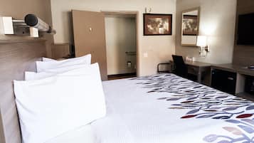 Ein Hotelzimmer mit einem großen Bett, einem Schreibtisch, einem Stuhl und einer Tür zu einem Badezimmer.