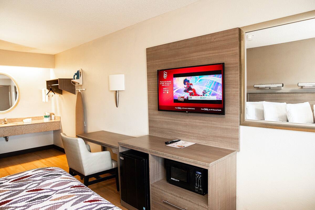 A hotel room with a bed, a desk, a microwave, a TV, and a mirror.