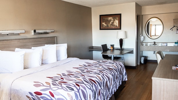 A hotel room with a bed, desk, chair, and a bathroom with a mirror and sink.