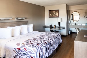 Quarto de hotel com cama, escrivaninha, cadeira e banheiro com espelho e pia.