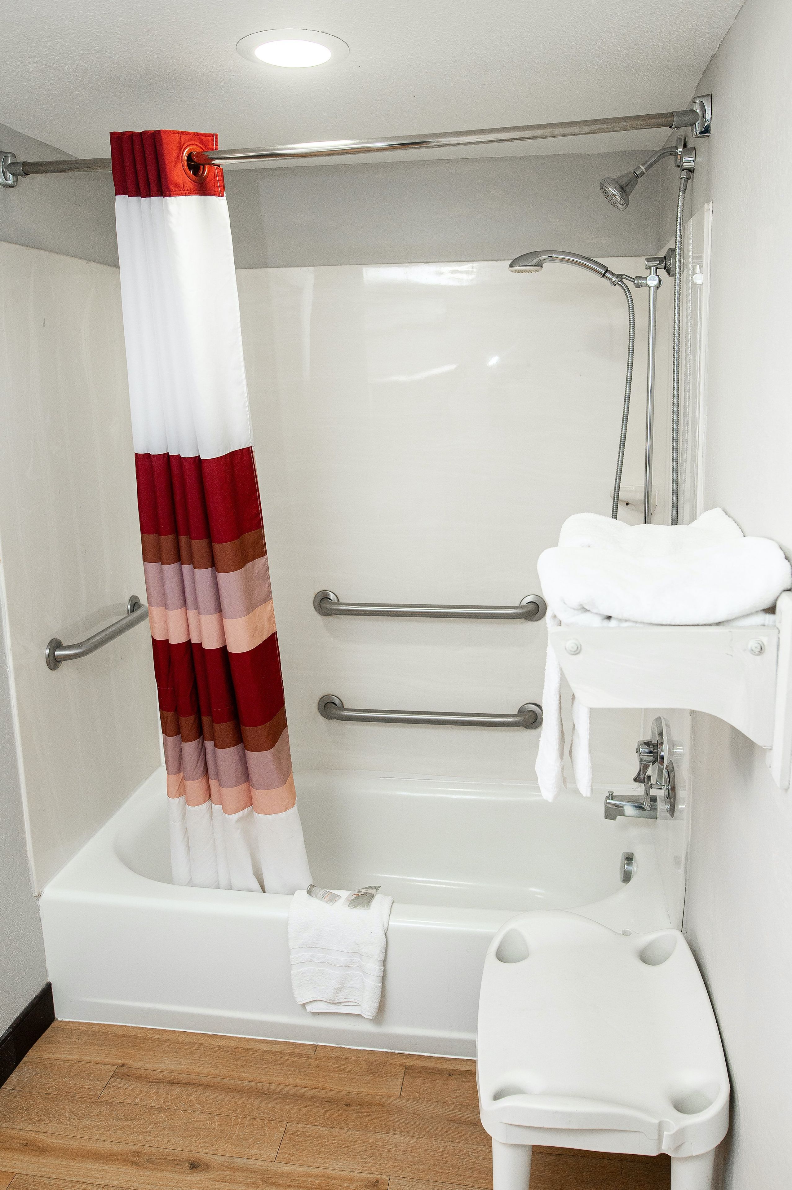 A bathroom with a white bathtub, a shower with a red and white striped curtain, a white sink with a towel rack, and a white toilet with a step.