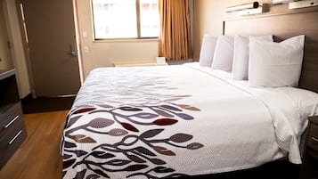 A hotel room with a bed, a dresser, a window with curtains, and a headboard with a light fixture.