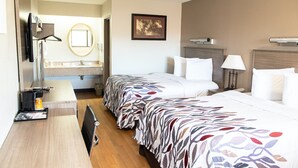 A hotel room with a bed, bedside table, lamp, and a framed picture on the wall. - Red Roof Inn Rochester - Henrietta (Henrietta)
