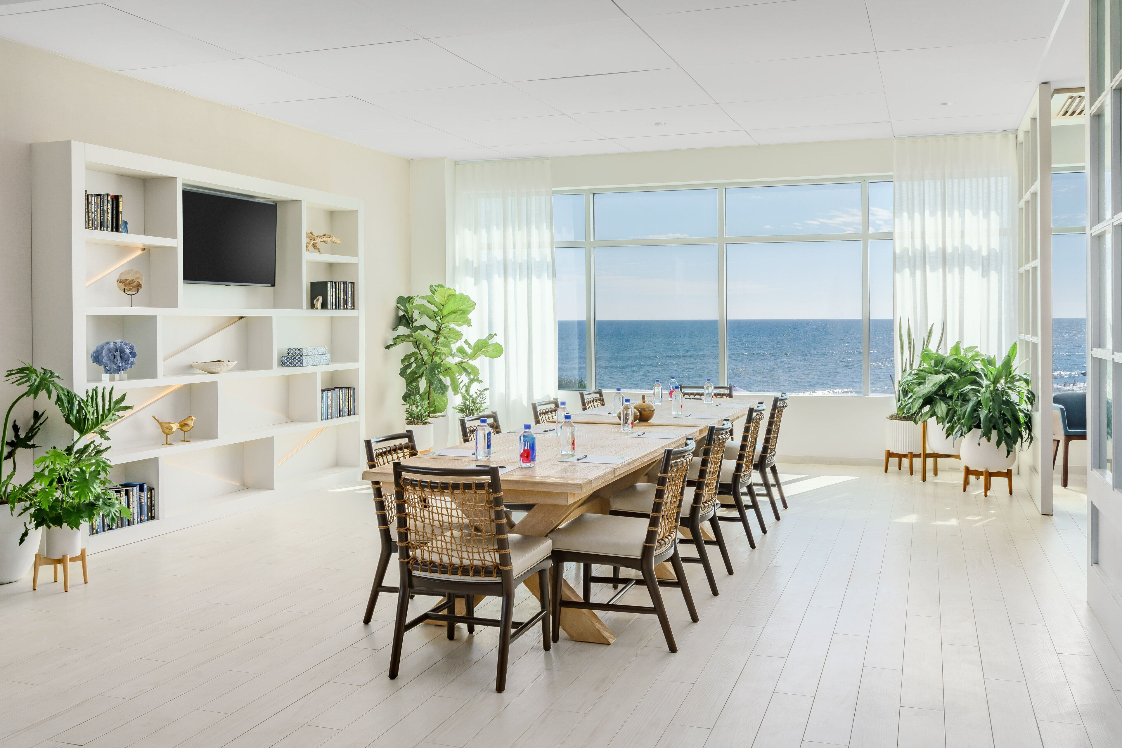 A spacious room with a large dining table, chairs, a television, and a bookshelf.