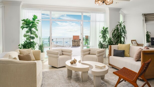 Amplia sala de estar con un gran ventanal con vista al mar, un balcón y varios muebles, incluyendo sofás y una mesa de centro.