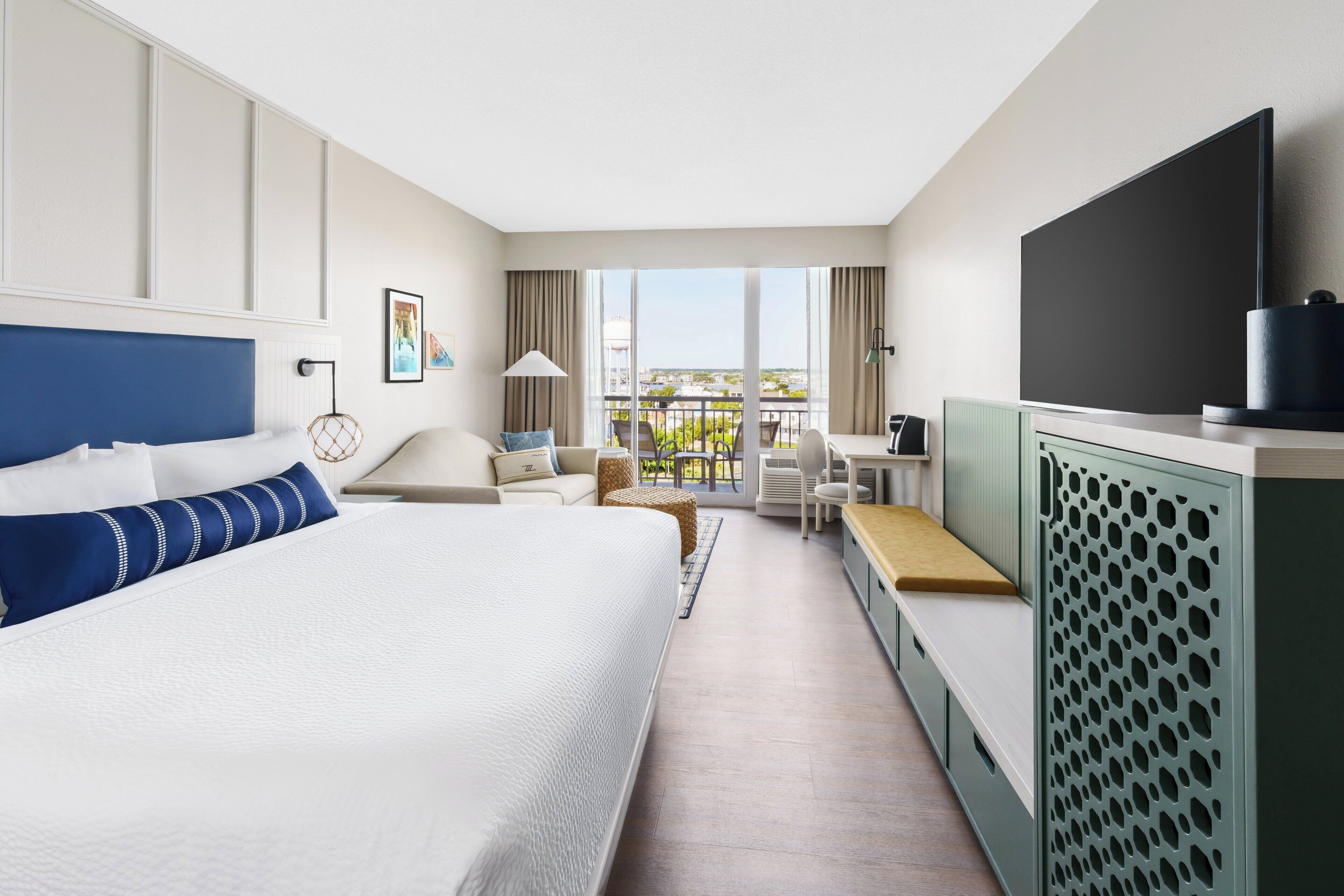 Ein Hotelzimmer mit einem großen Bett, einem Schreibtisch, einem Stuhl, einem Fernseher und einem Balkon mit Blick.