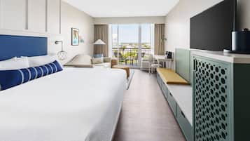 Ein Hotelzimmer mit einem großen Bett, einem Schreibtisch, einem Stuhl, einem Fernseher und einem Balkon mit Blick.