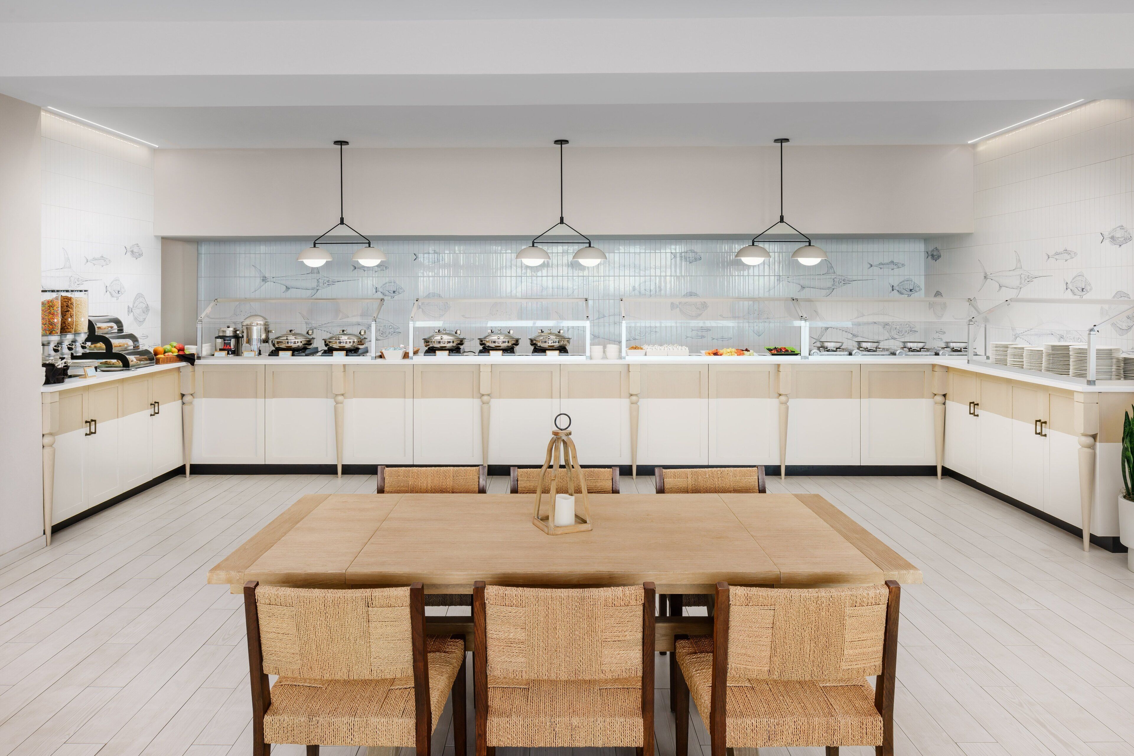 A modern kitchen with a central island, white cabinetry, and a dining area with wicker chairs.