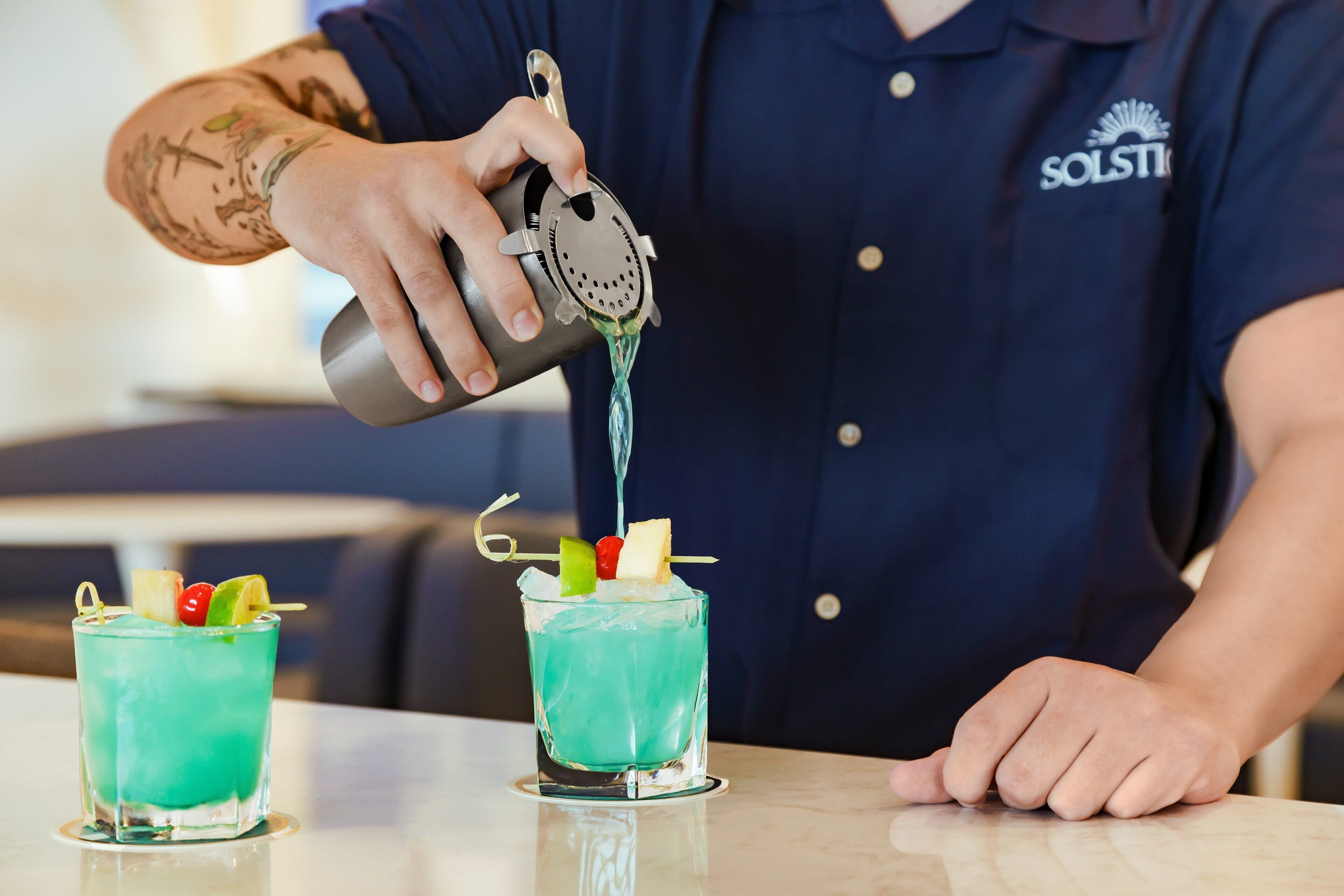 A bartender pouring a blue drink into a glass with fruit garnishes.