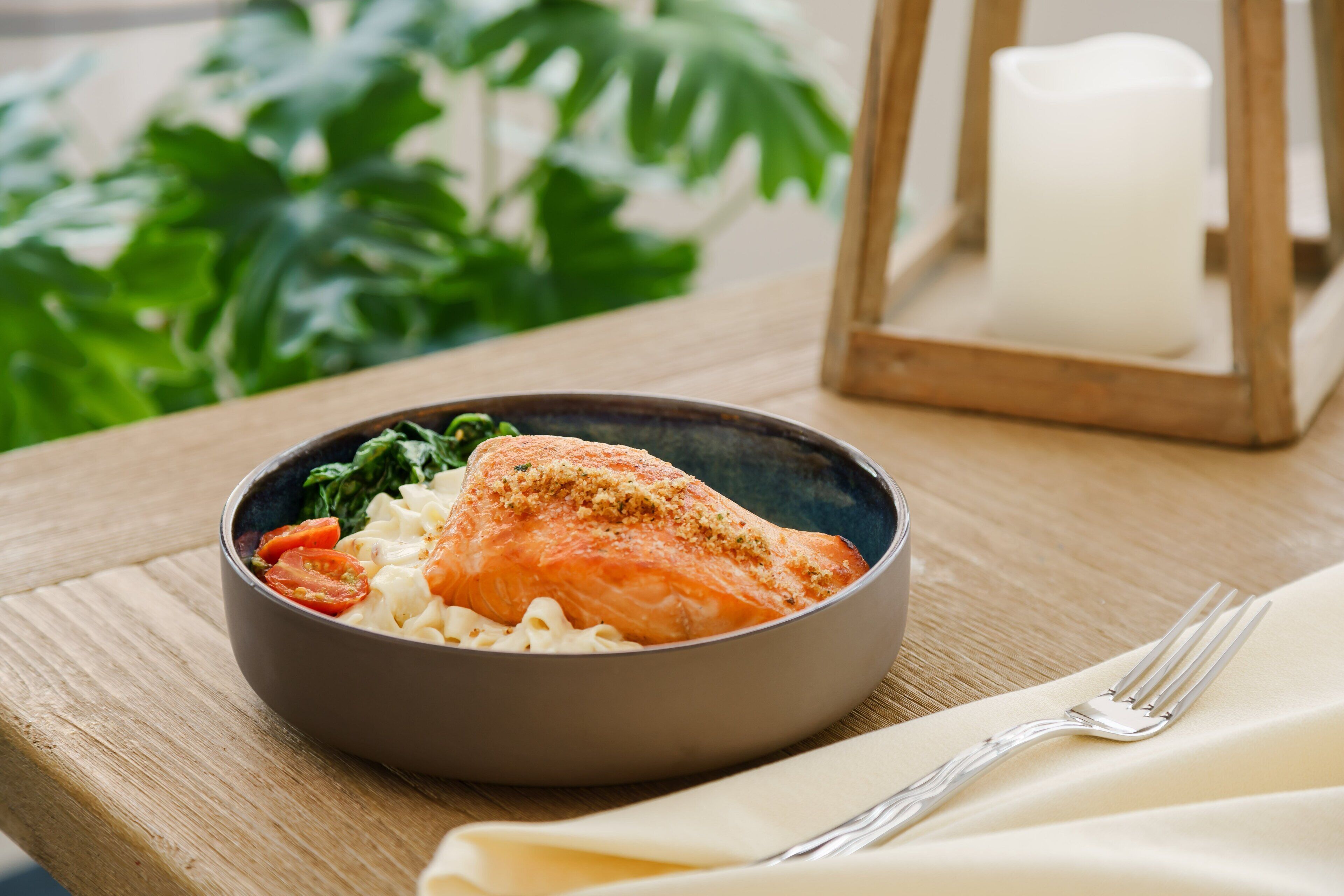 Una ciotola di cibo con salmone, pasta e verdure su un tavolo di legno.
