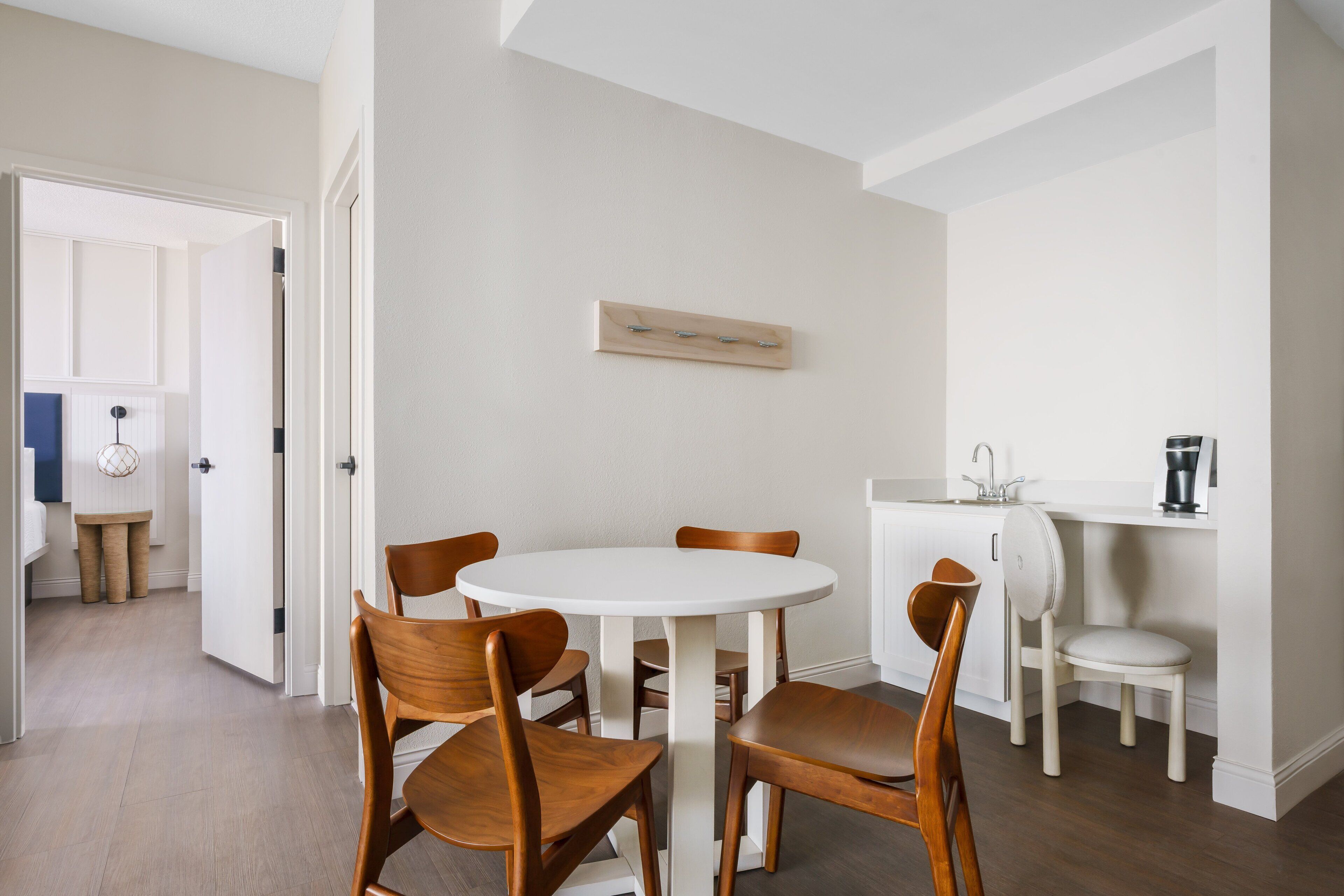 A dining area with a round white table, wooden chairs, and a white cabinet with a sink.