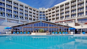Un hotel con una piscina amplia, varios balcones y zonas de estar al aire libre.