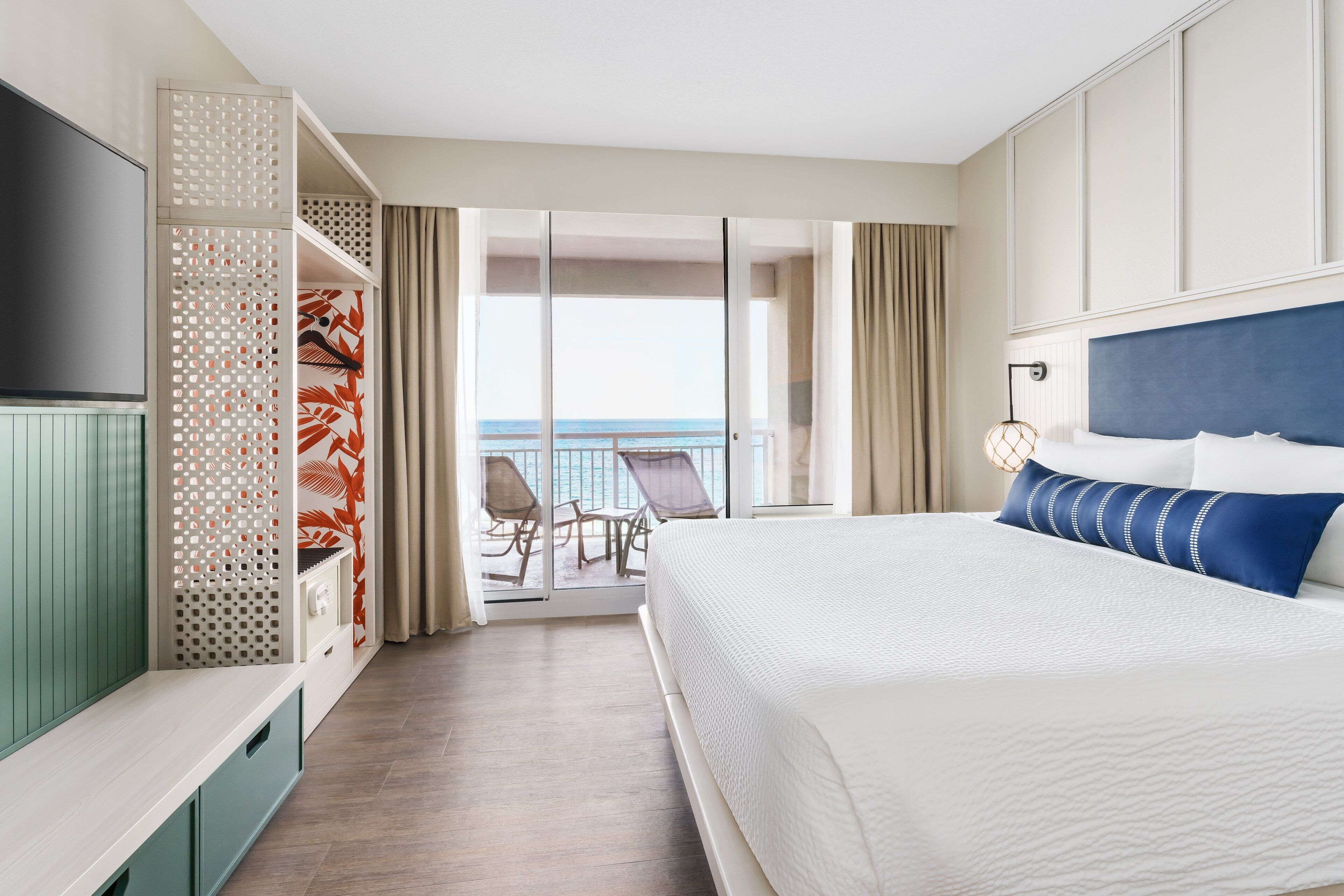 Ein Hotelzimmer mit einem großen Bett, einem Fernseher, einem Balkon mit Meerblick und einer Sitzecke mit Sesseln.