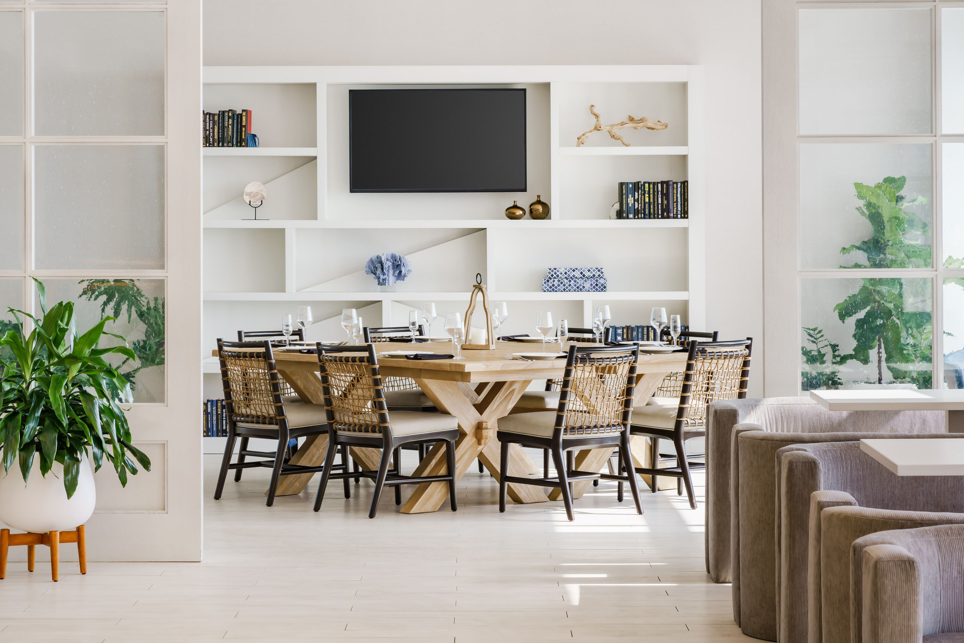 A dining area with a wooden table and chairs, surrounded by white shelving with books and decorative items.