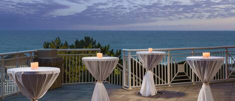 A terrace with four round tables, each with a candle, overlooking the sea.