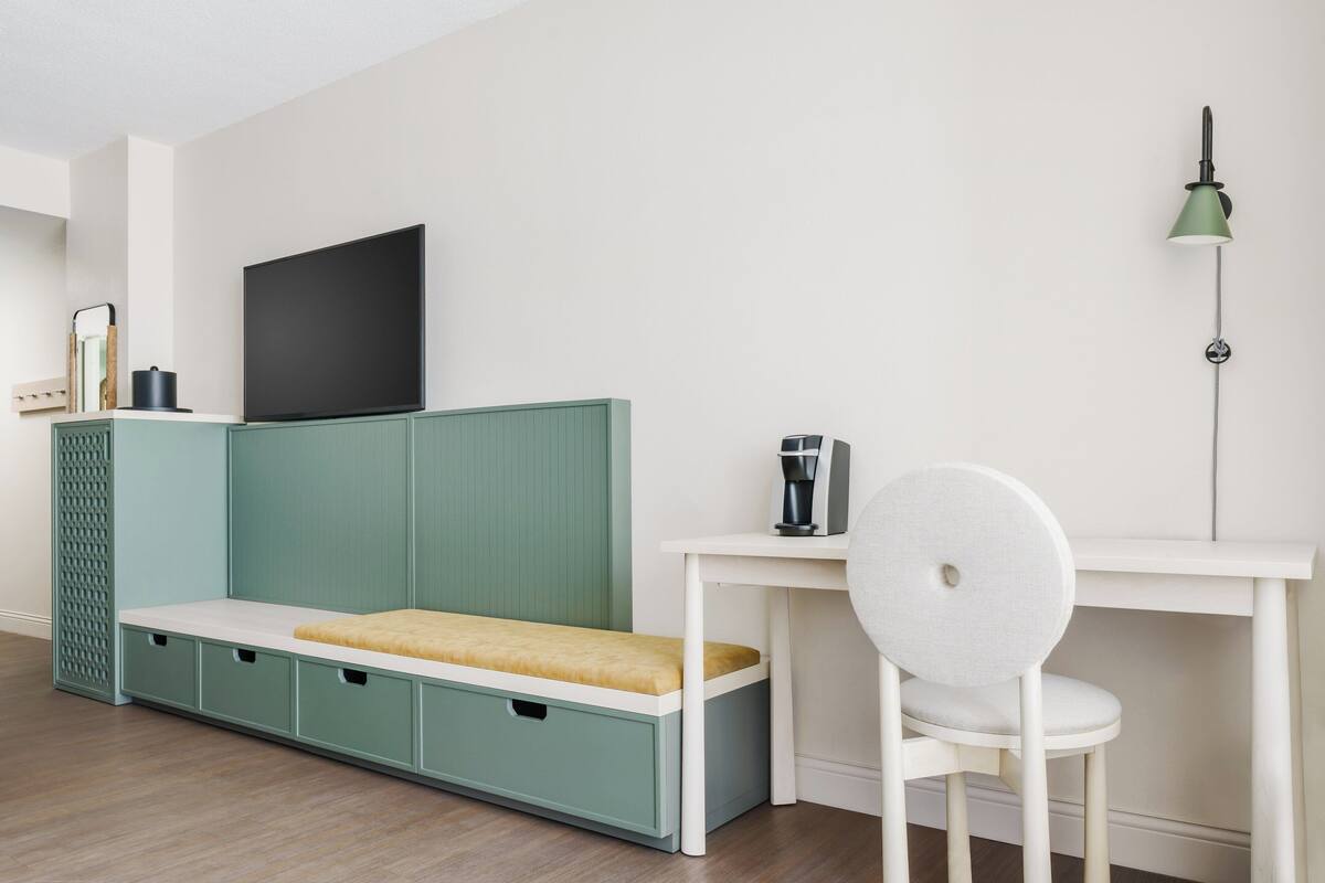 Ein modernes Kinderzimmer mit einer grünen Aufbewahrungseinheit, einem weißen Schreibtisch, einem Stuhl, einem Fernseher und einer grünen Stehlampe.