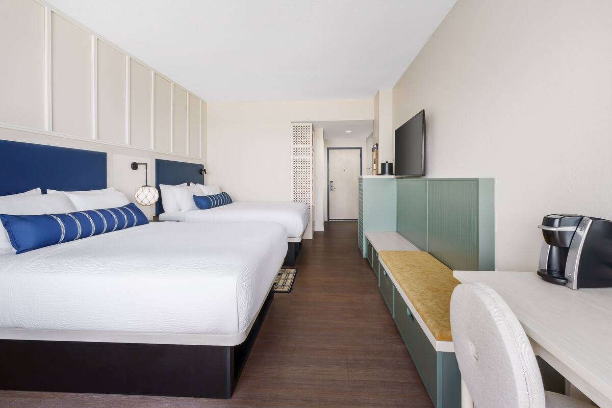 Ein Hotelzimmer mit zwei Betten, einem Schreibtisch, einer Kaffeemaschine und einem Fernseher.