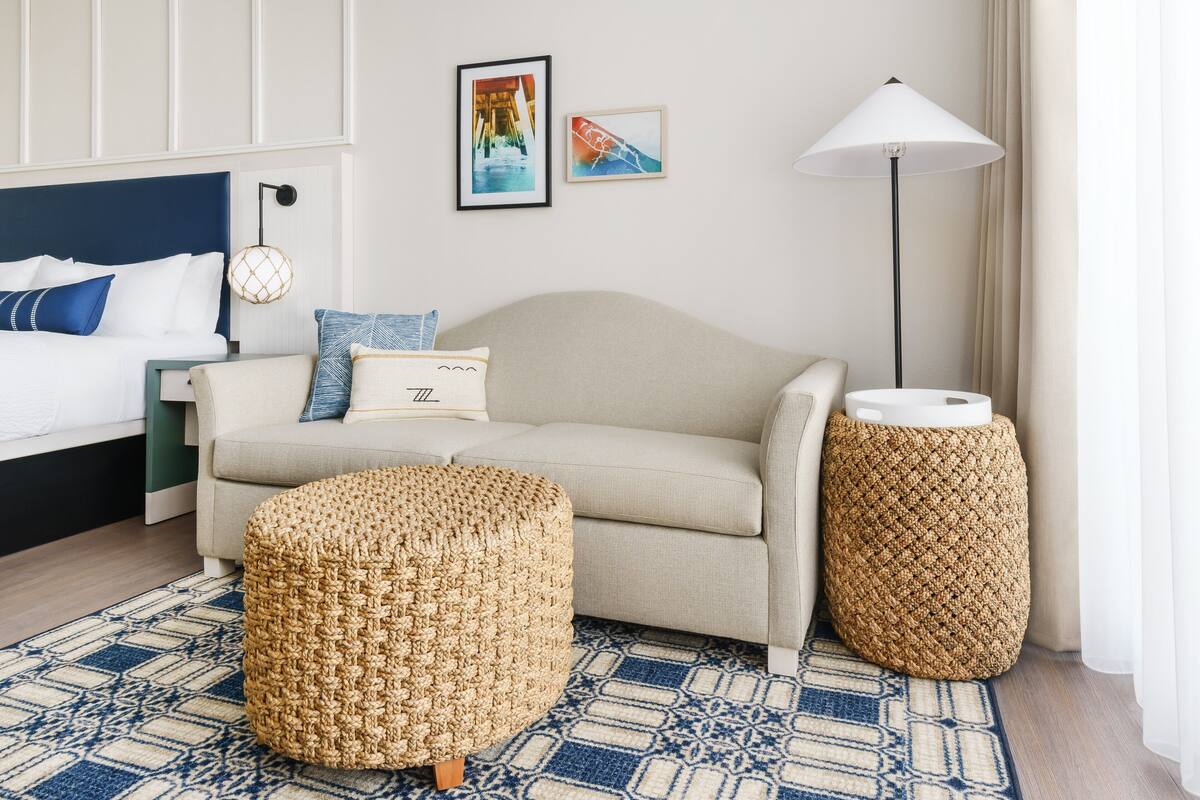 Ein modernes Schlafzimmer mit einem Bett, einer Couch, zwei gewebten Hocker, einer Stehlampe und zwei gerahmten Bildern an der Wand.