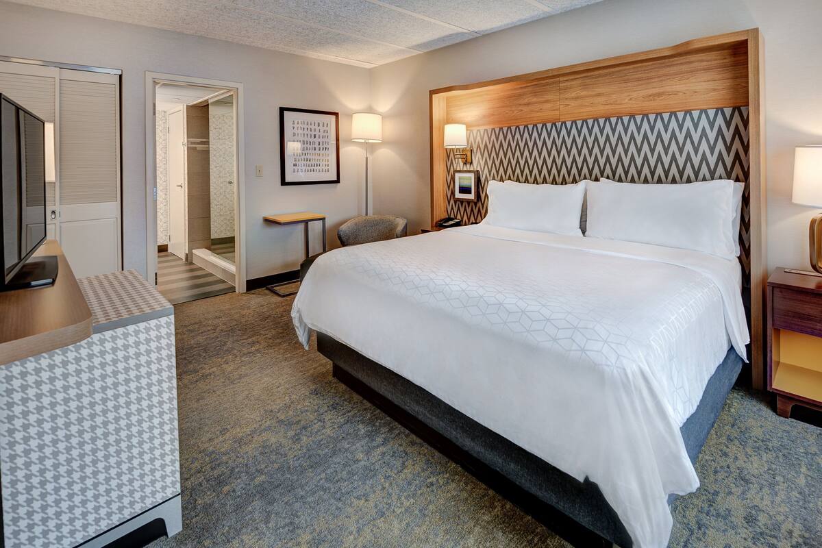 A hotel room with a large bed, a wooden headboard, a desk, and a chair.
