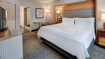 A hotel room with a large bed, a wooden headboard, a desk, and a chair.