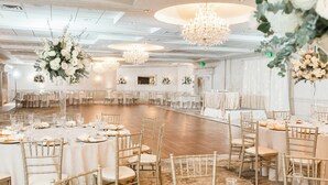 A large, elegantly decorated banquet hall with round tables, gold chairs, and hanging floral arrangements.