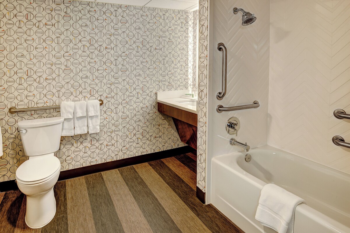 A modern bathroom with a toilet, sink, and bathtub, featuring patterned wallpaper and a herringbone floor.