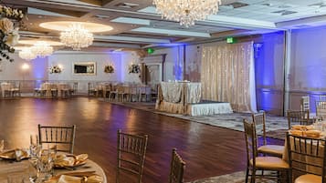 Un salón de banquetes con mesas redondas, sillas, candelabros y arreglos florales.